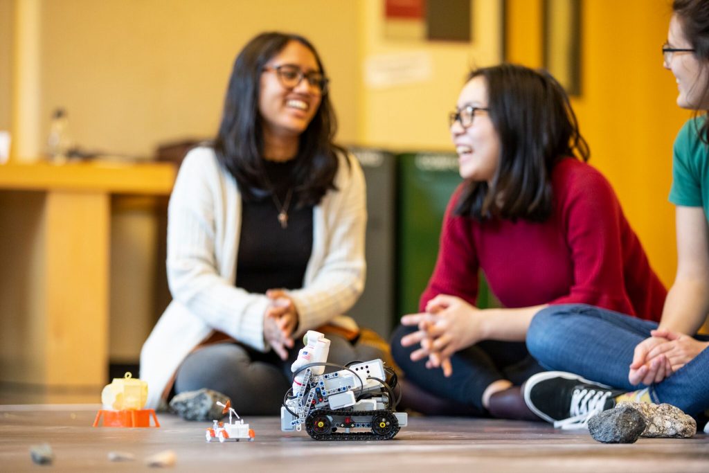 These University of Washington students demonstrate the challenge involving a lunar lander (left, orange) a Lego Mindstorms robot (center) and rock samples (right).